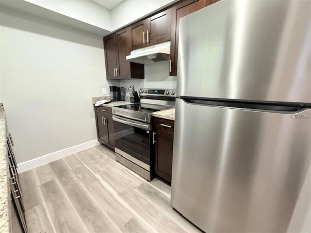 A kitchen features dark wood cabinets, stainless steel appliances, and light-colored wood-look flooring — 332 AVENUE D SE, WINTER HAVEN, FL