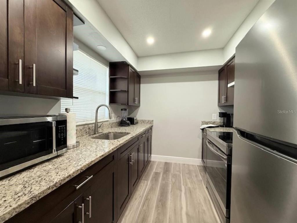 A galley kitchen features dark wood cabinets, granite countertops, and stainless steel appliances — 332 AVENUE D SE, WINTER HAVEN, FL