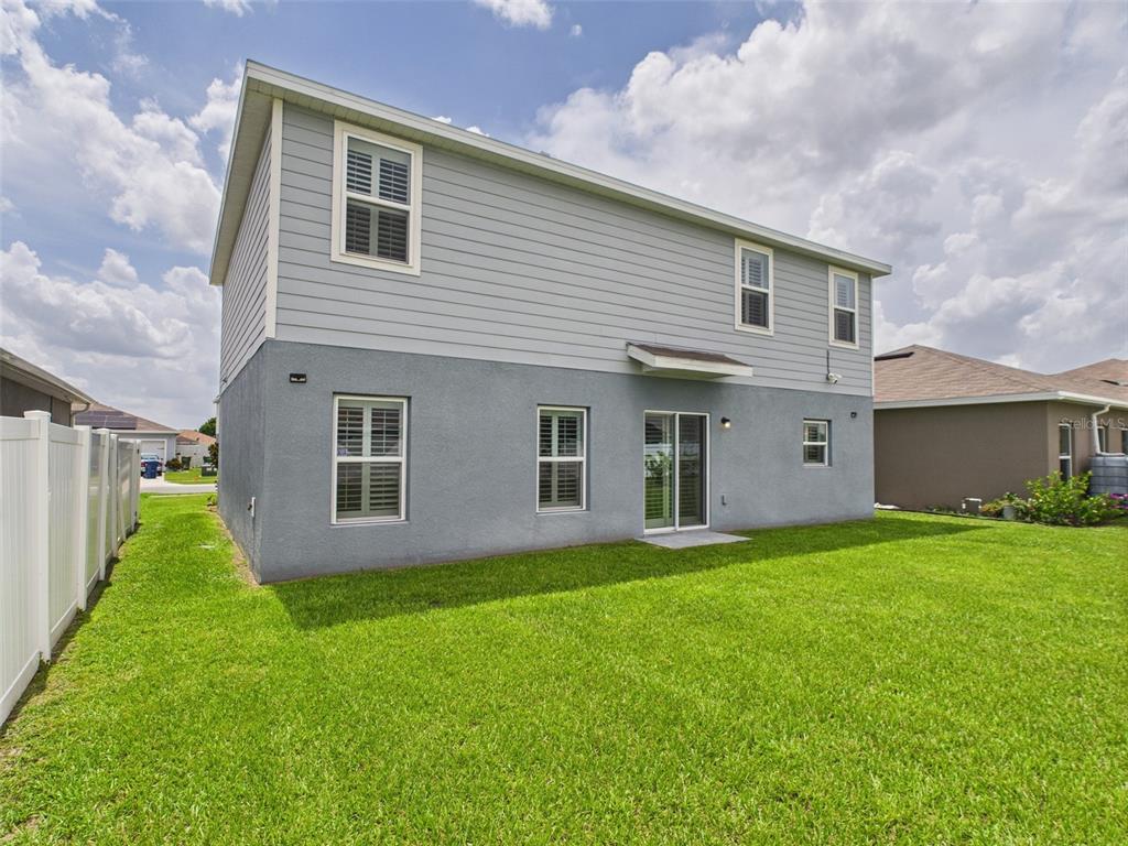 The rear exterior of a two-story house features gray siding, stucco walls, and a lawn — 567 EAGLE LANDING BOULEVARD, WINTER HAVEN, FL