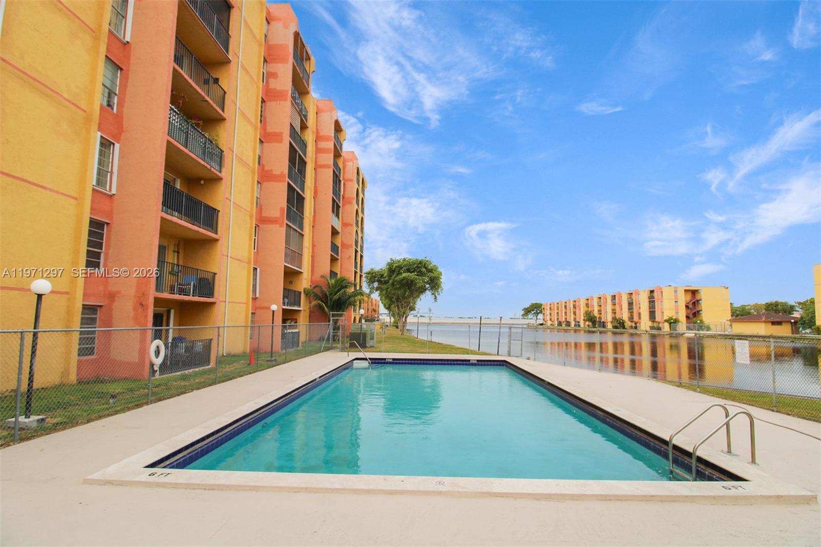 A rectangular swimming pool sits beside a multi-story apartment building and a lake — 4717 NW 7th St # 10, Miami FL 33126, MIAMI, FL