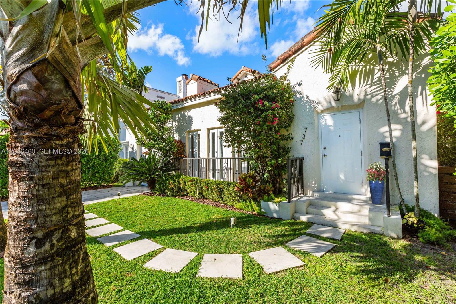 A white stucco house with a tiled roof features a front lawn and stone walkway — 737 Alhambra Cir, Coral Gables FL 33134, CORAL GABLES, FL