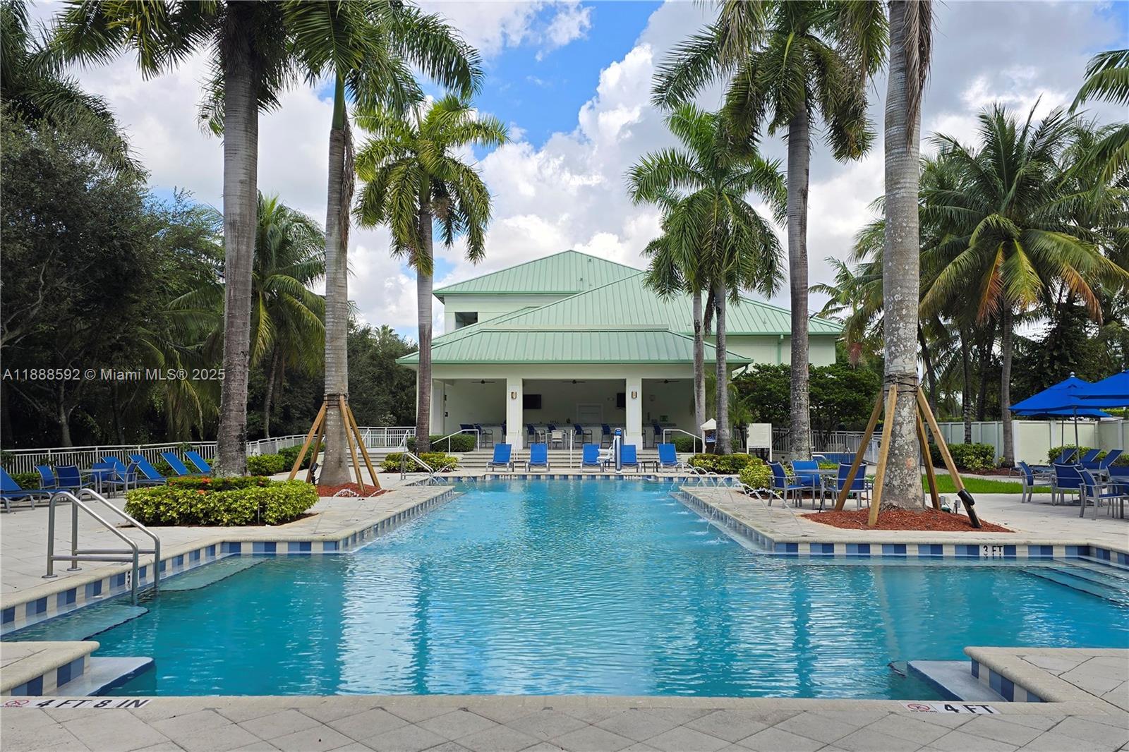 A rectangular swimming pool sits in front of a clubhouse with a green metal roof — 5300 NW 87th Ave # 1212, Doral FL 33178, DORAL, FL