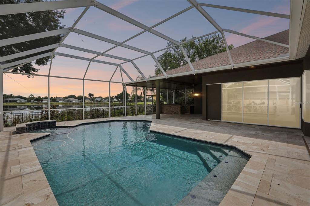 A swimming pool with a screened enclosure overlooks a lake at sunset — 15720 BEREA DRIVE, ODESSA, FL