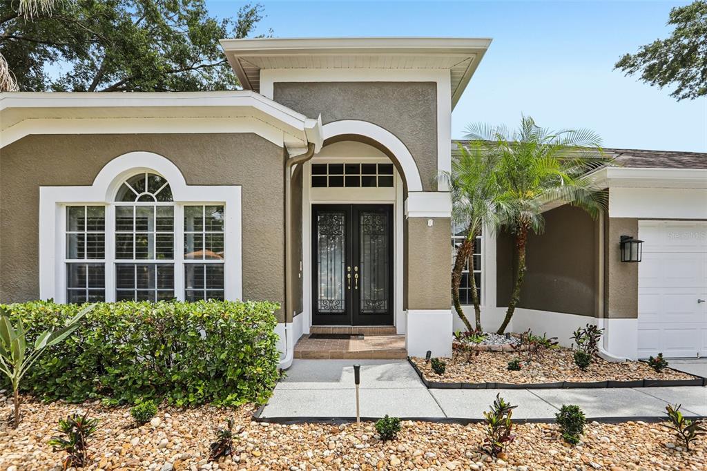 The exterior of a single-story home features a tan stucco facade, arched entryway, and double doors — 15720 BEREA DRIVE, ODESSA, FL