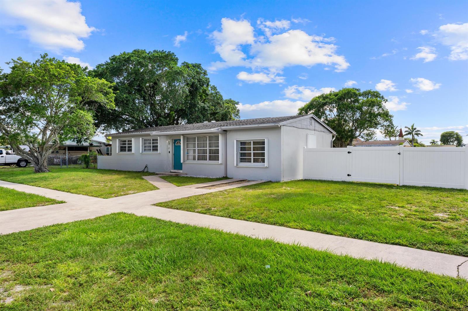 A single-story gray house with a teal front door sits on a grassy lot — 153 Abaco Drive, Palm Springs FL 33461, PALM SPRINGS, FL