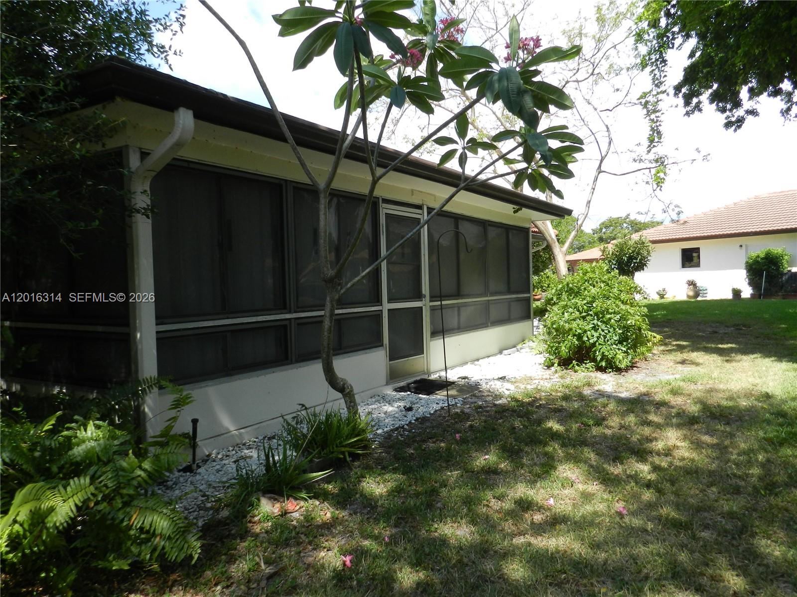 A screened-in porch with a metal door sits next to a tree and lawn — 305 NW 42nd St, Boca Raton FL 33431, BOCA RATON, FL