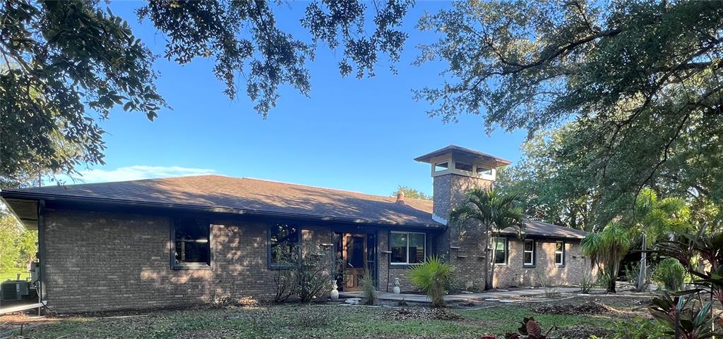 A single-story brick house features a prominent chimney structure and is surrounded by mature trees — 3190 ALOE STREET, PUNTA GORDA, FL