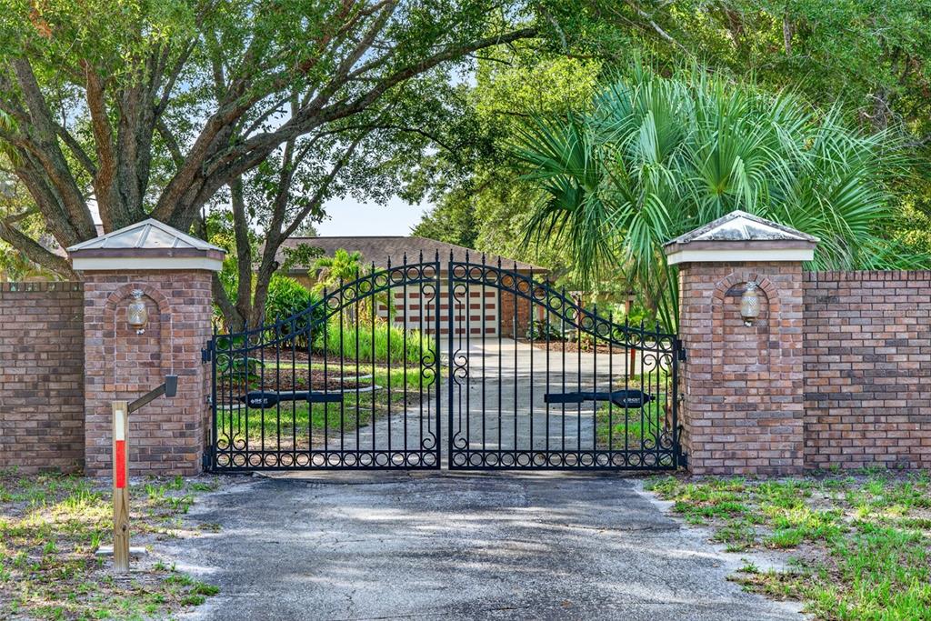 A black metal gate stands between two brick pillars at the entrance of a driveway — 3190 ALOE STREET, PUNTA GORDA, FL