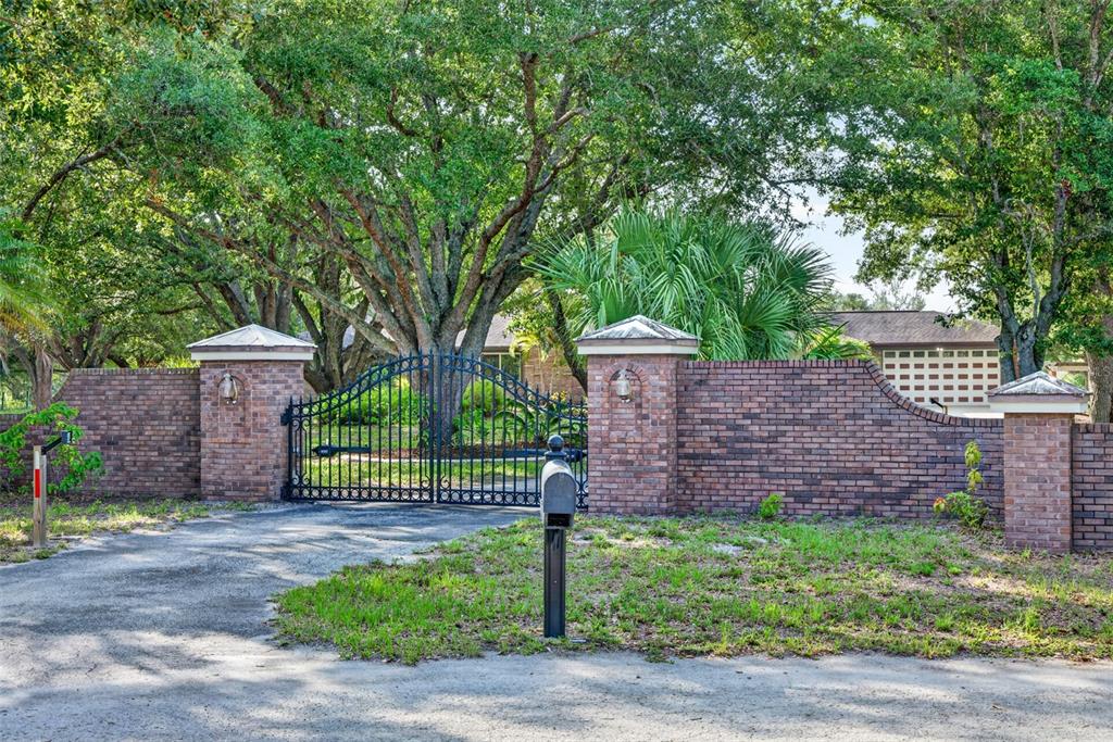 A brick wall with a metal gate and a mailbox stands in front of trees — 3190 ALOE STREET, PUNTA GORDA, FL
