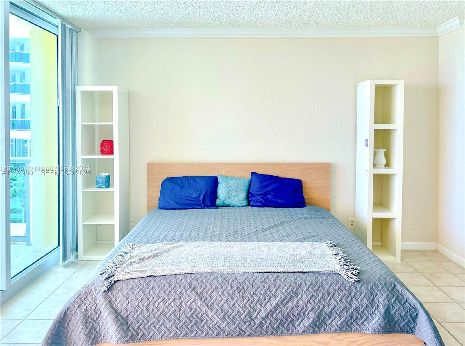 A bedroom features a bed with blue pillows, two white shelving units, and a sliding door — 2501 S Ocean Dr # 424, Hollywood FL 33019, HOLLYWOOD, FL
