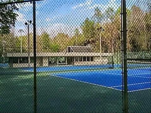 A view through a chain-link fence of a blue tennis court and a clubhouse building — 119 TOMOKA TRAIL UNIT 119, LONGWOOD, FL