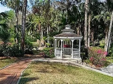 A white wooden gazebo sits in a landscaped garden with a brick walkway and trees — 119 TOMOKA TRAIL UNIT 119, LONGWOOD, FL