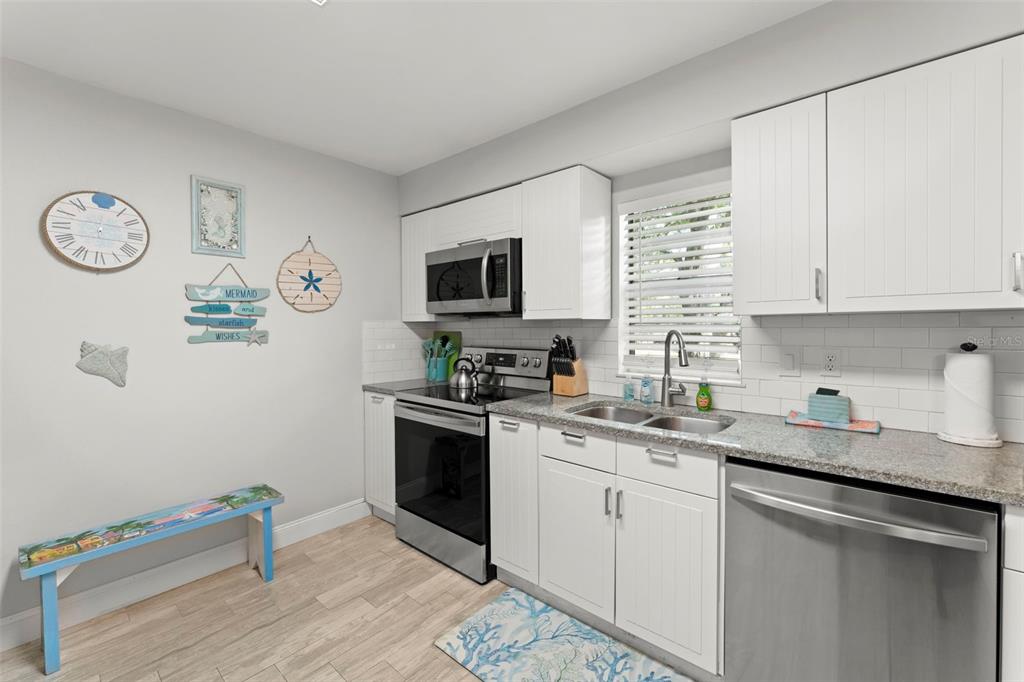 A kitchen features white cabinets, stainless steel appliances, granite countertops, and a beach-themed decor — 328 PERSHING STREET, DUNEDIN, FL
