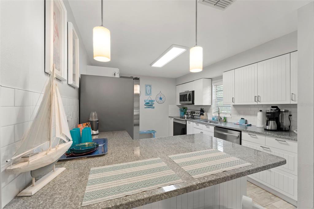 A kitchen features a granite breakfast bar, white cabinetry, stainless steel appliances, and pendant lighting — 328 PERSHING STREET, DUNEDIN, FL
