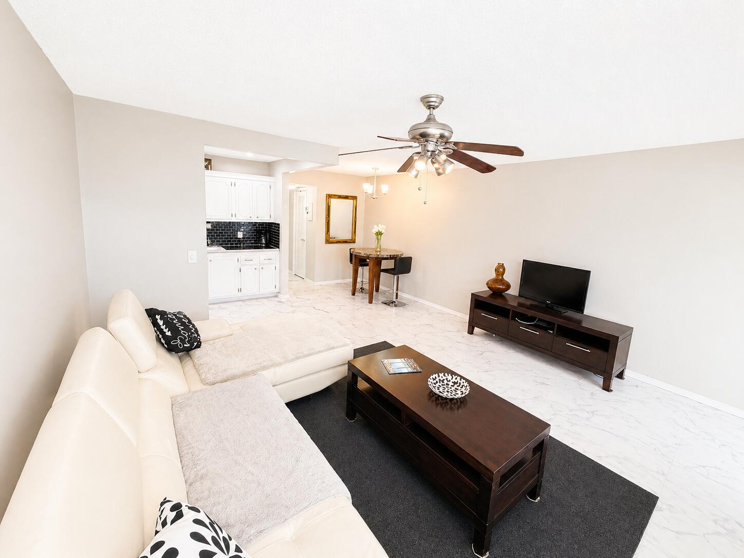 A living room with a white sectional sofa, dark wood coffee table, and marble-look flooring — 140 Ventnor # I, Deerfield Beach FL 33442, DEERFIELD BEACH, FL