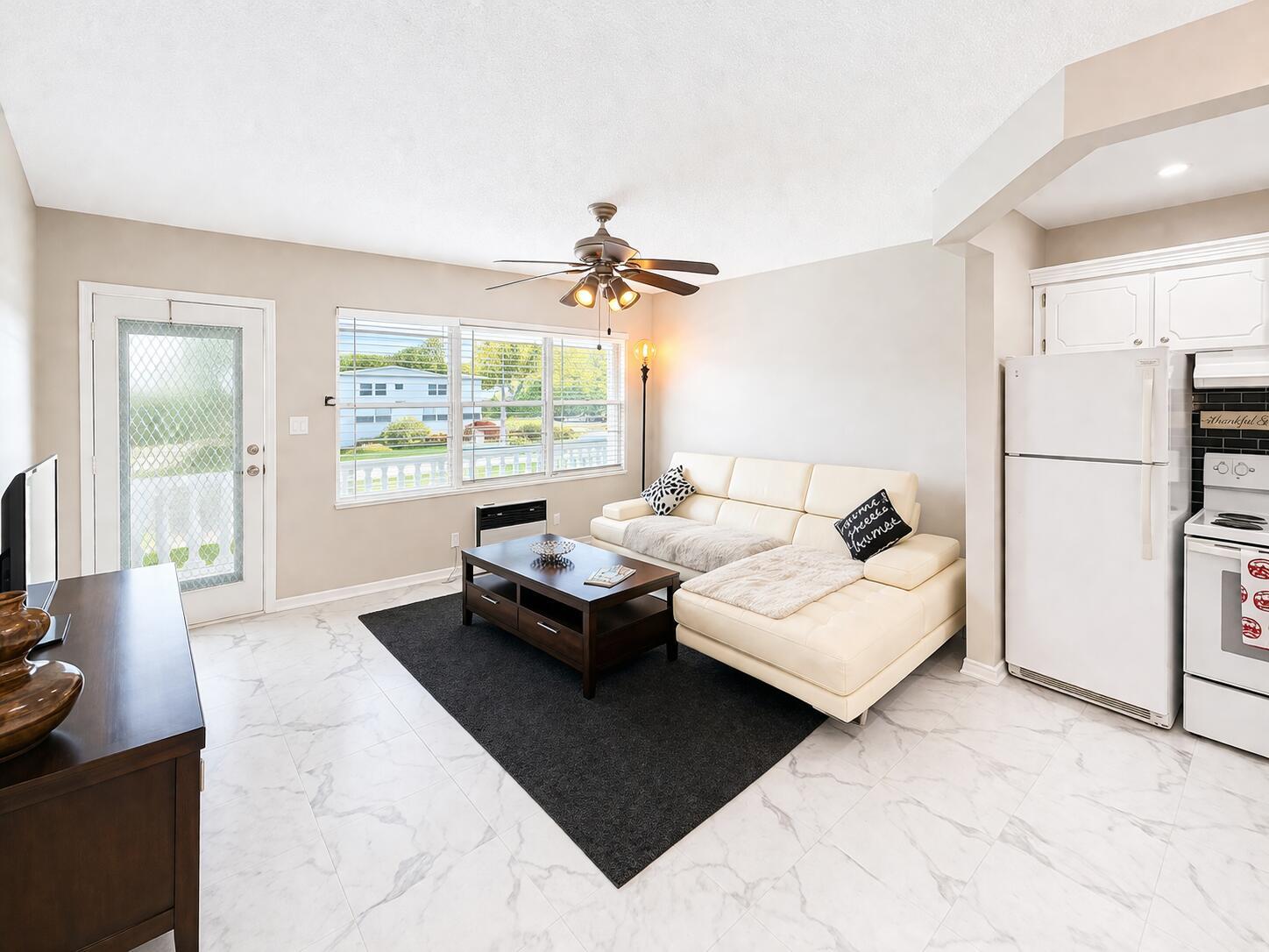 A living room with white tile floors, a white sectional sofa, and an adjacent kitchen — 140 Ventnor # I, Deerfield Beach FL 33442, DEERFIELD BEACH, FL