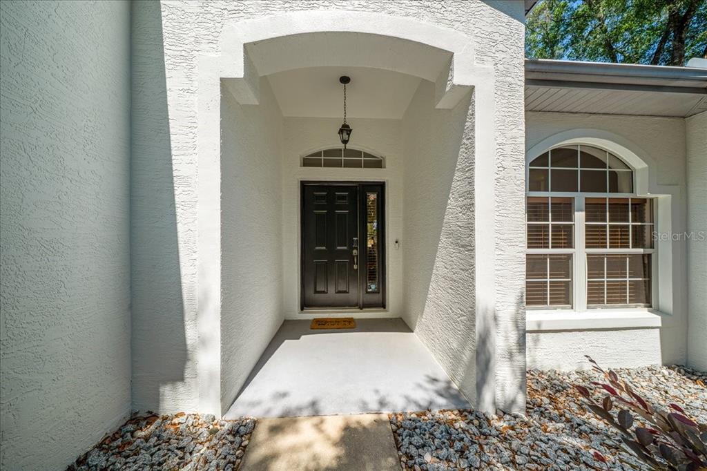 A white stucco house exterior features a dark front door under a recessed entryway — 8859 SW 196TH AVENUE ROAD, DUNNELLON, FL