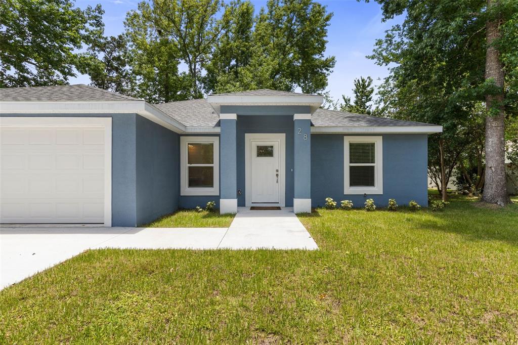 A blue single-story house features a white front door, a garage, and a concrete walkway — 28 WOODSTON LANE, PALM COAST, FL