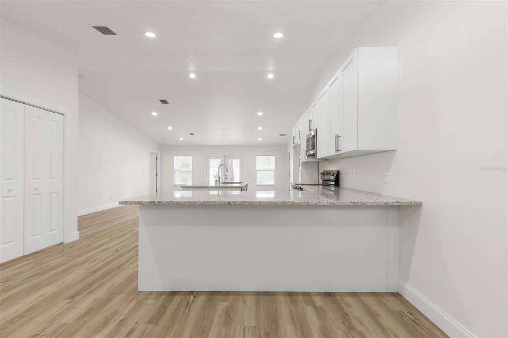 A modern kitchen features white cabinets, granite countertops, and light wood-look flooring — 28 WOODSTON LANE, PALM COAST, FL