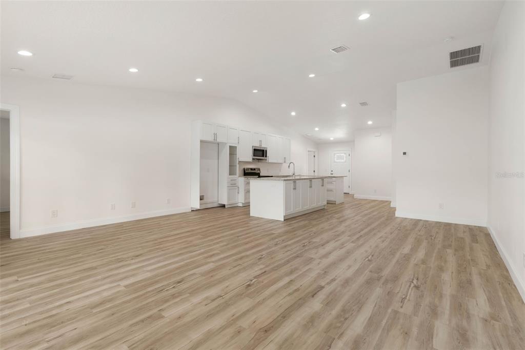 A bright, open-concept kitchen and living area featuring white cabinetry, an island, and wood-look flooring — 28 WOODSTON LANE, PALM COAST, FL