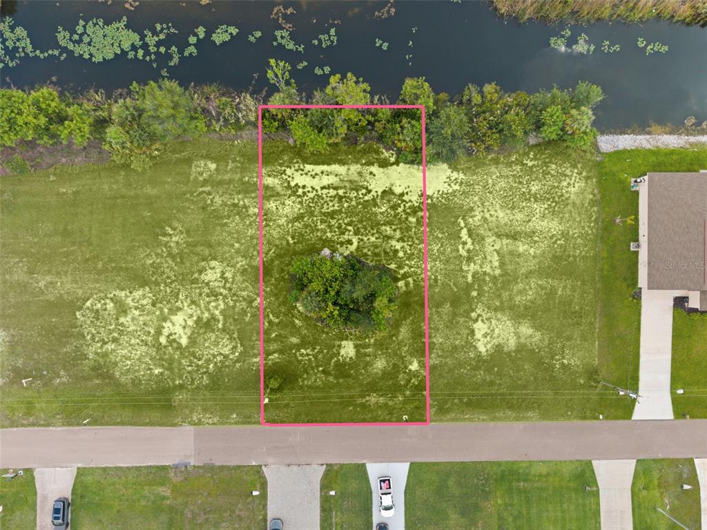 An aerial view shows a rectangular vacant lot outlined in pink bordering a body of water — 907 NE 32ND TERRACE, CAPE CORAL, FL