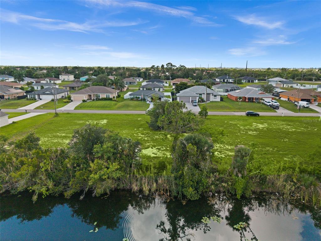 An aerial view shows a grassy lot situated between a residential street and a pond — 907 NE 32ND TERRACE, CAPE CORAL, FL