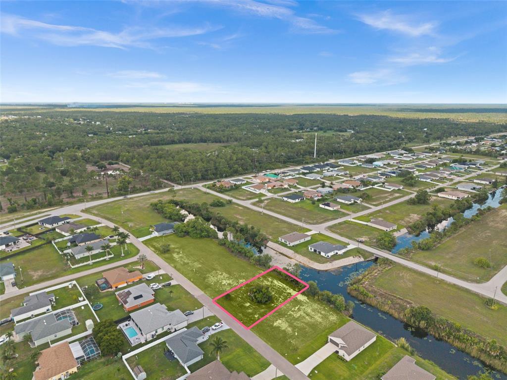 An aerial view shows a vacant, rectangular residential lot outlined in pink near a canal — 907 NE 32ND TERRACE, CAPE CORAL, FL