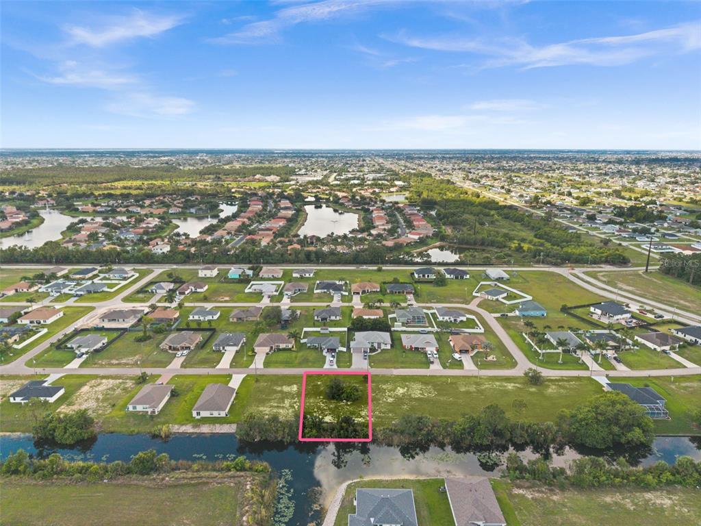 An aerial view shows a vacant, rectangular residential lot highlighted in pink along a canal — 907 NE 32ND TERRACE, CAPE CORAL, FL