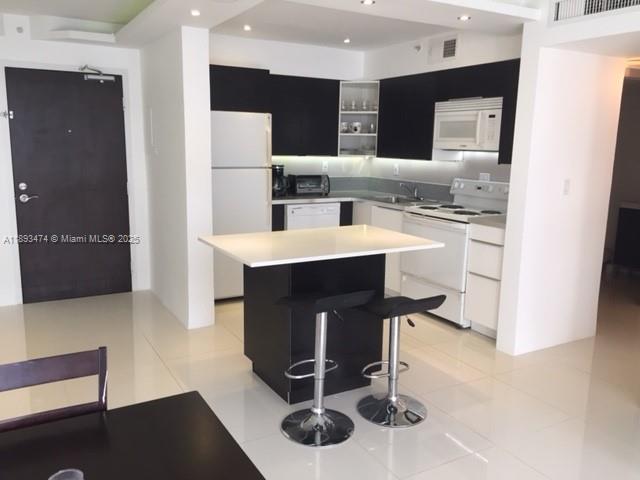 A modern kitchen features dark cabinetry, white appliances, a central island, and two bar stools — 1500 Bay Rd # 758S, Miami Beach FL 33139, MIAMI BEACH, FL