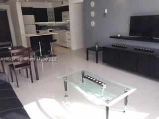 A modern open-concept living room features a glass coffee table, dark furniture, and tiled floors — 1500 Bay Rd # 758S, Miami Beach FL 33139, MIAMI BEACH, FL