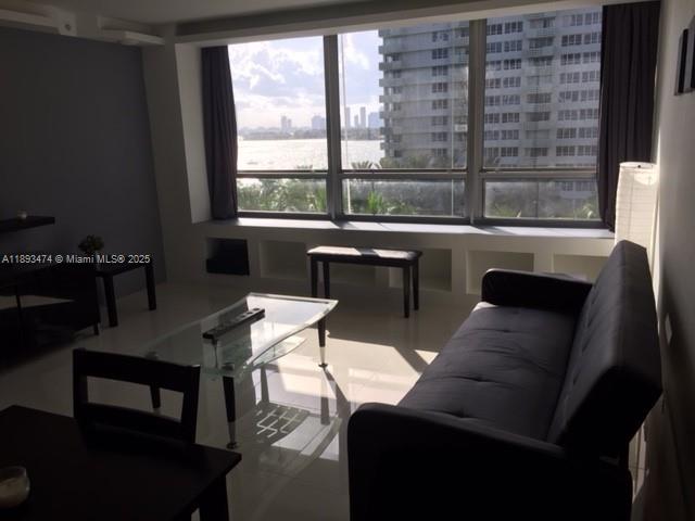 A living room with a dark sofa, glass coffee table, and large windows overlooking water — 1500 Bay Rd # 758S, Miami Beach FL 33139, MIAMI BEACH, FL