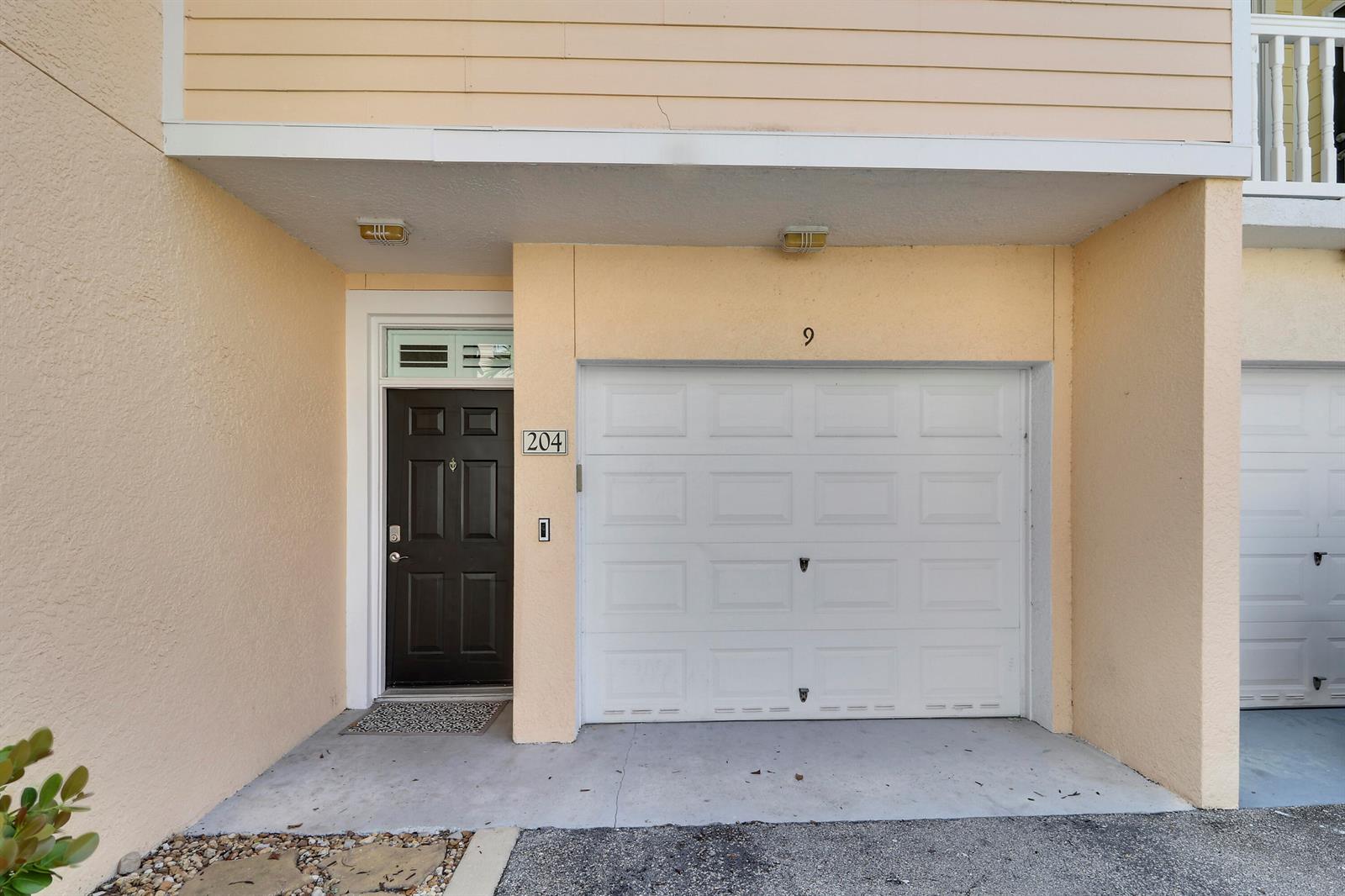 The exterior of a townhouse features a dark front door, a white garage door, and light-colored siding — 155 Galicia Way # 204, Jupiter FL 33458, JUPITER, FL