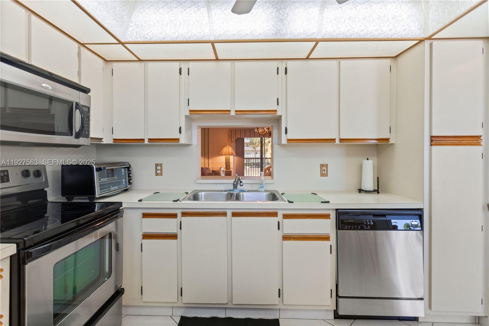A kitchen features white cabinets with wood trim, stainless steel appliances, and a pass-through window — 190 SE 5th Ave # 202, Dania Beach FL 33004, DANIA BEACH, FL