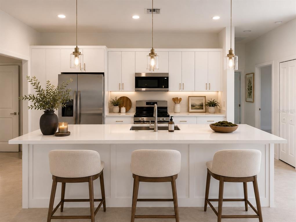 A modern white kitchen features a large island with three stools and stainless steel appliances — 3114 23 STREET W, LEHIGH ACRES, FL