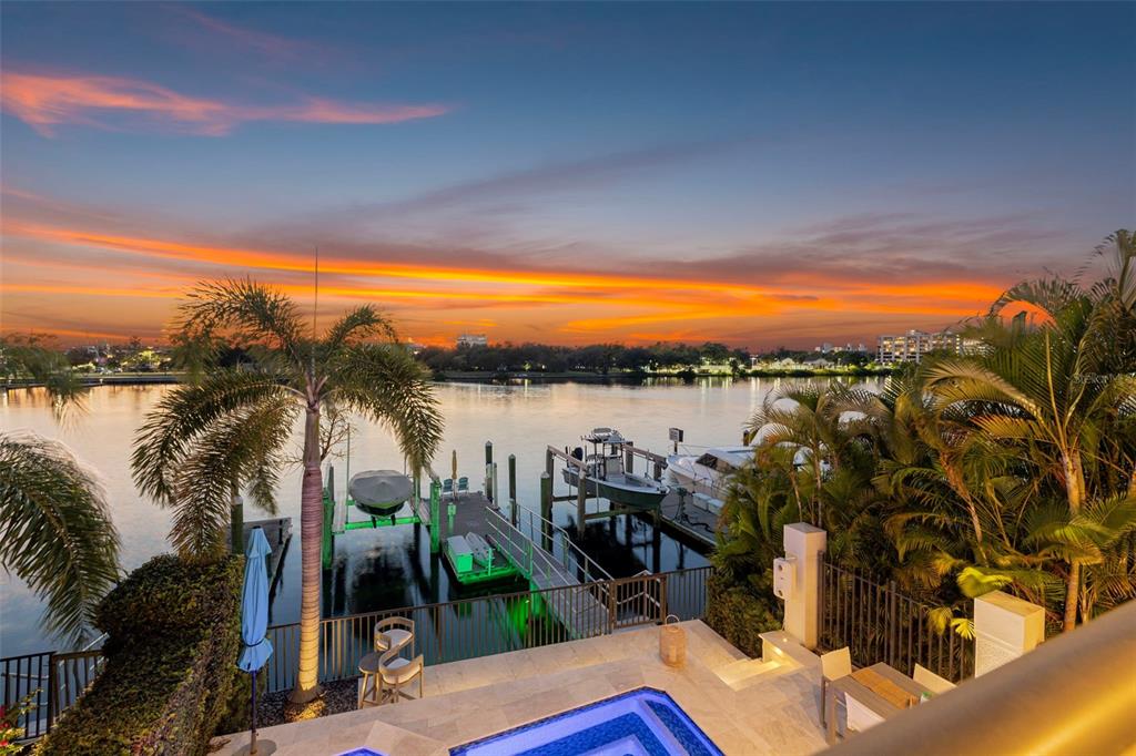 An elevated view of a waterfront patio with a pool, boat dock, and sunset sky — 1009 ROYAL PASS ROAD, TAMPA, FL