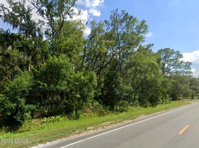 A wooded, undeveloped lot sits alongside a paved road under a blue sky — 2884 W NEW YORK AVENUE, DELAND, FL