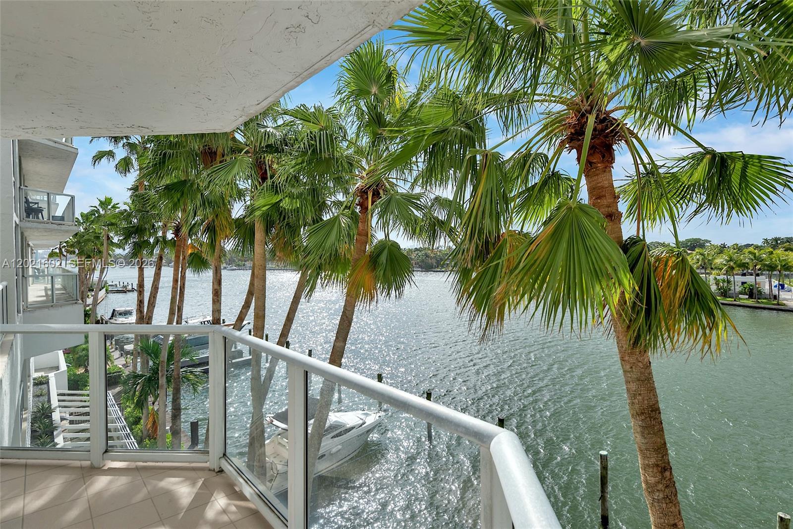 A balcony view overlooks a waterway with palm trees and a docked boat — 5900 Collins Ave # 408, Miami Beach FL 33140, MIAMI BEACH, FL