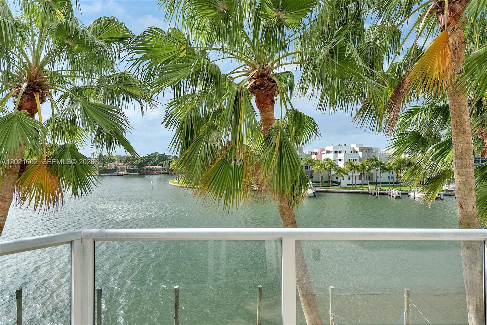 A balcony with a glass railing overlooks a canal lined with palm trees and houses — 5900 Collins Ave # 408, Miami Beach FL 33140, MIAMI BEACH, FL