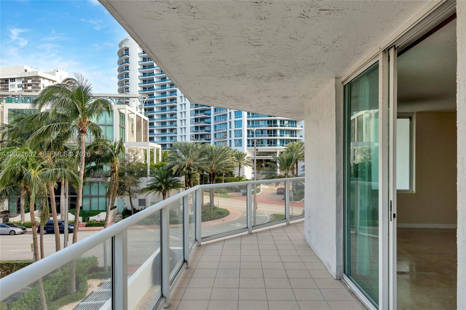 A balcony with tile flooring and a glass railing overlooks a street and high-rise buildings — 5900 Collins Ave # 408, Miami Beach FL 33140, MIAMI BEACH, FL