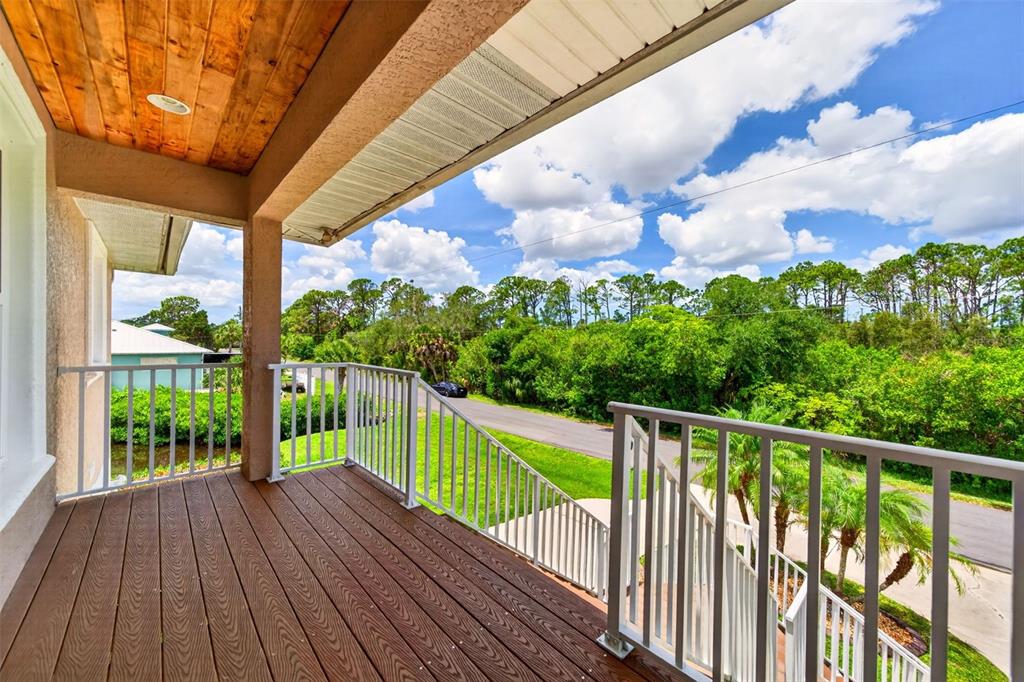 An elevated wooden deck features white railings and a wood-paneled ceiling overlooking a suburban street — 9050 CALOOSA DRIVE, VENICE, FL