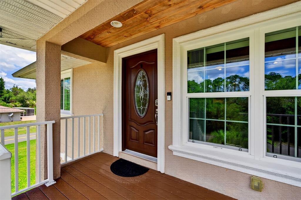 A covered front porch features a wood-plank ceiling, a brown door, and white railings — 9050 CALOOSA DRIVE, VENICE, FL