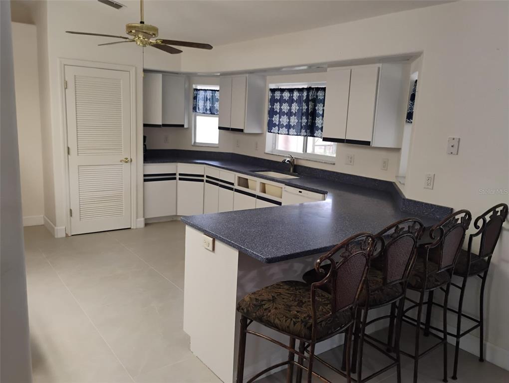 A kitchen features white cabinets, blue countertops, a breakfast bar with stools, and tile flooring — 5905 CLEVELAND DRIVE, PUNTA GORDA, FL