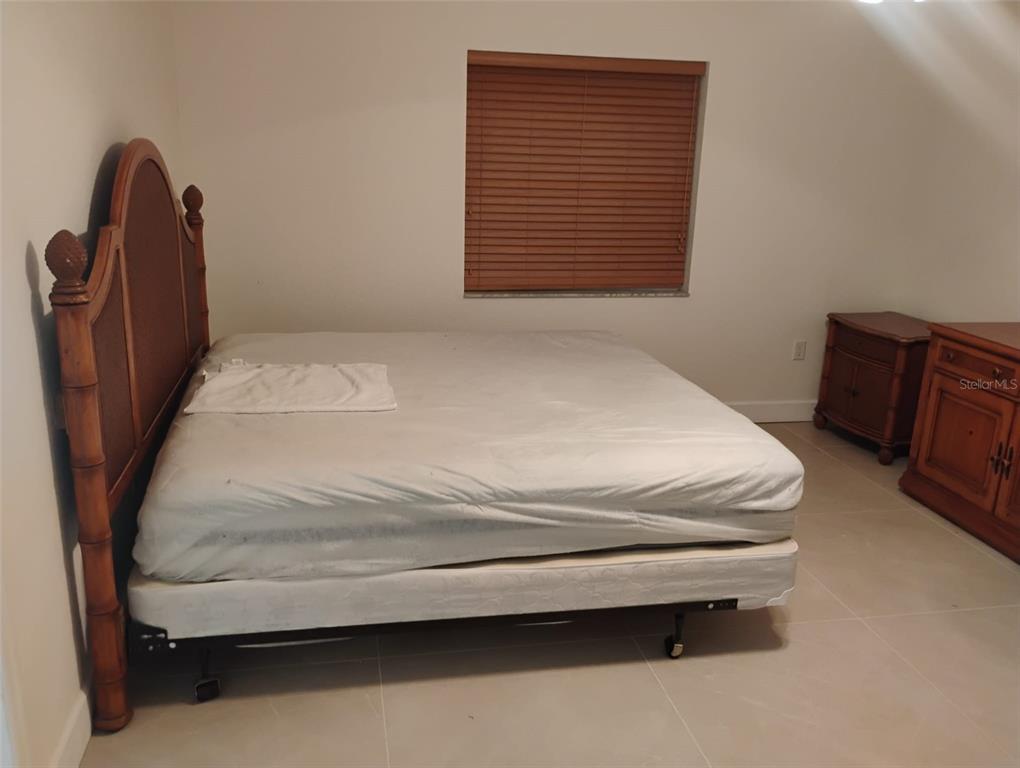 A bedroom features a large bed with a wooden headboard, tile flooring, and a window — 5905 CLEVELAND DRIVE, PUNTA GORDA, FL