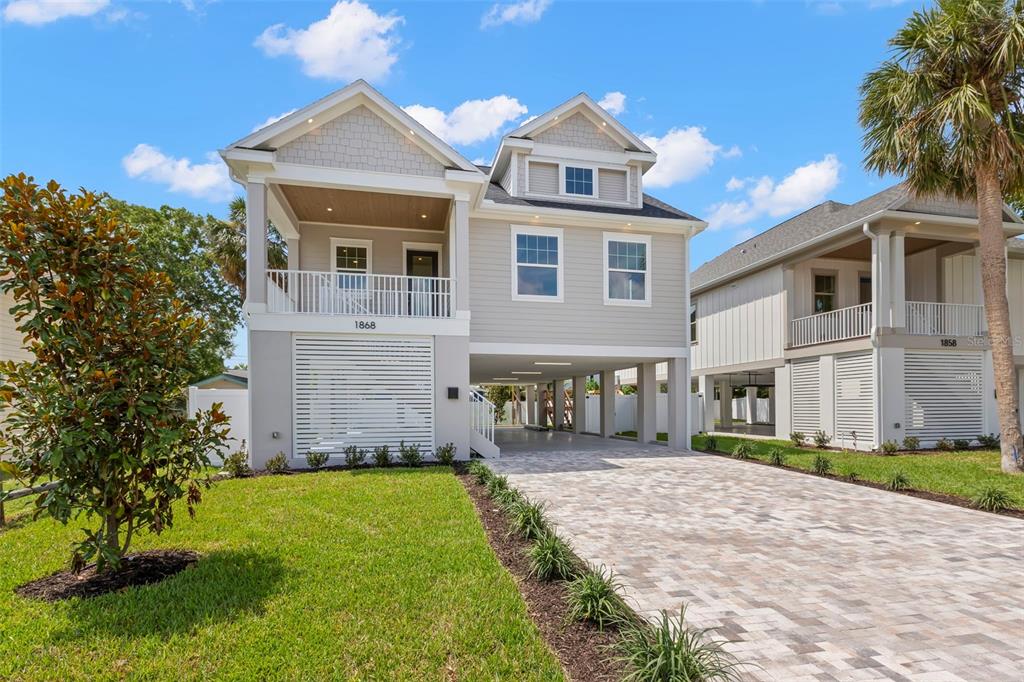 A two-story house on stilts features light gray siding, a paved driveway, and a porch — 1868 MISSISSIPPI AVENUE NE, ST PETERSBURG, FL