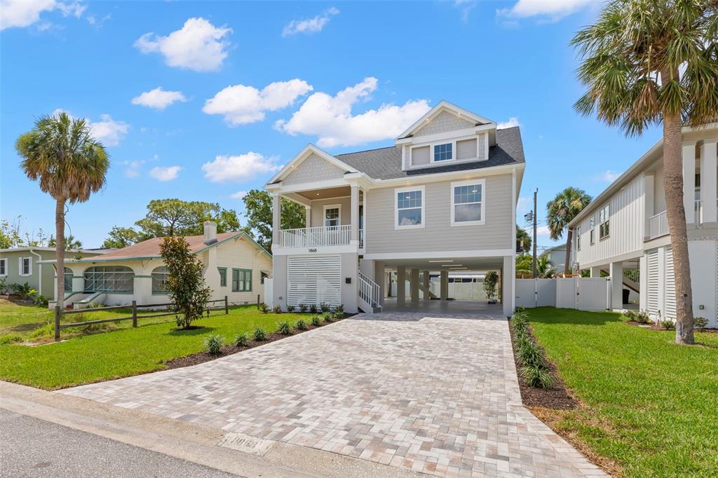 A two-story elevated house with light gray siding and a paved driveway under a blue sky — 1868 MISSISSIPPI AVENUE NE, ST PETERSBURG, FL