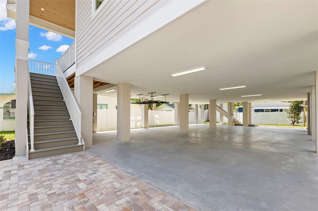 A large, open-air concrete parking area sits beneath an elevated house with stairs — 1868 MISSISSIPPI AVENUE NE, ST PETERSBURG, FL