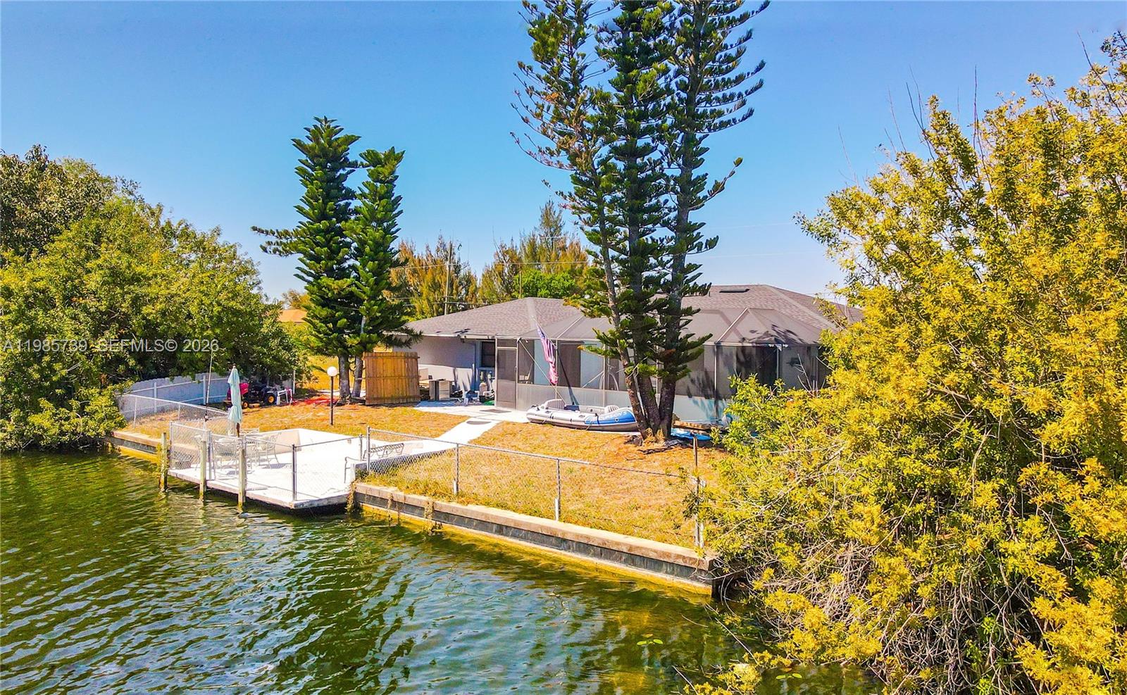 A waterfront house features a screened-in patio, a private dock, and tall pine trees — 2908 NW 9TH TER, Cape Coral FL 33993, CAPE CORAL, FL