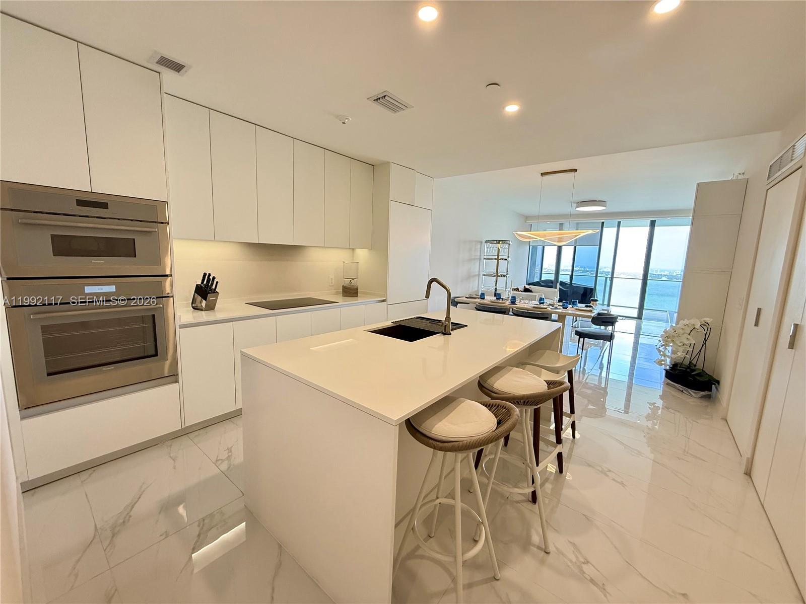 A modern white kitchen features a central island, stainless steel appliances, and marble-look flooring — 700 NE 24 street # 3802, Miami FL 33137, MIAMI, FL
