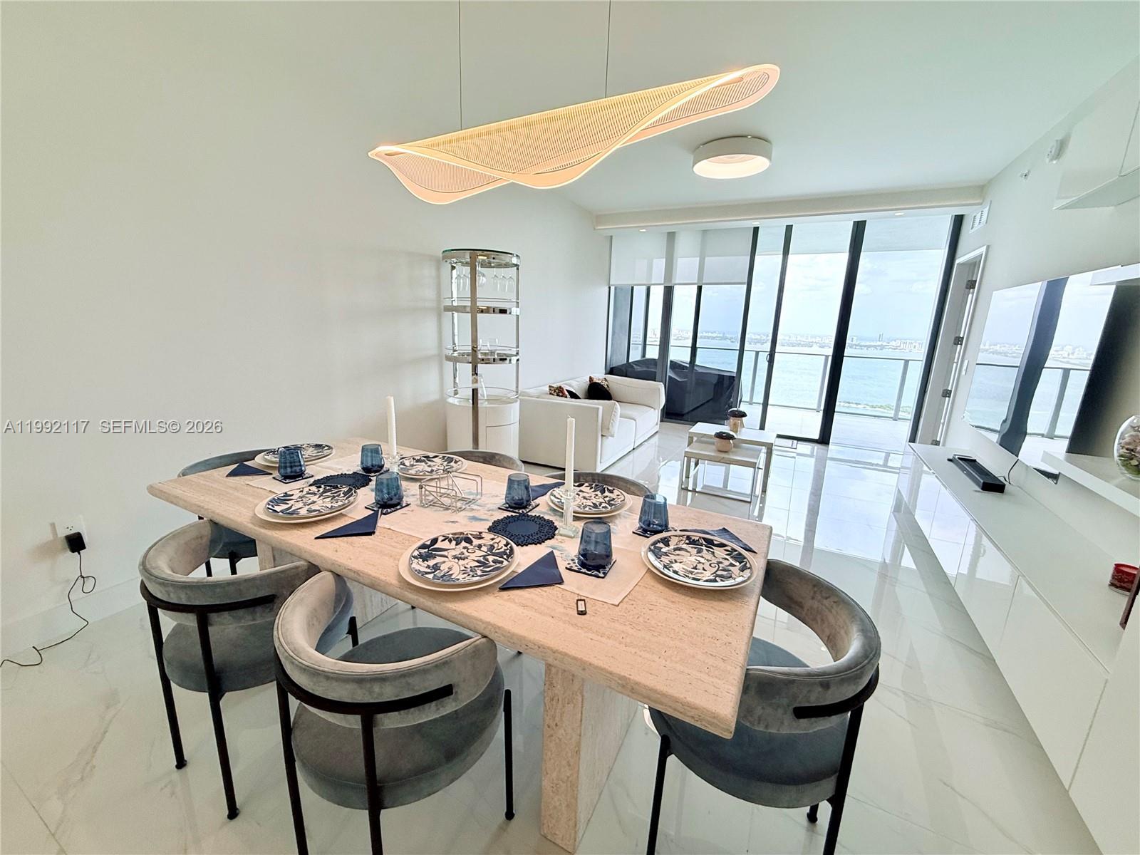 A dining area with a stone table and blue chairs overlooks a balcony and water — 700 NE 24 street # 3802, Miami FL 33137, MIAMI, FL