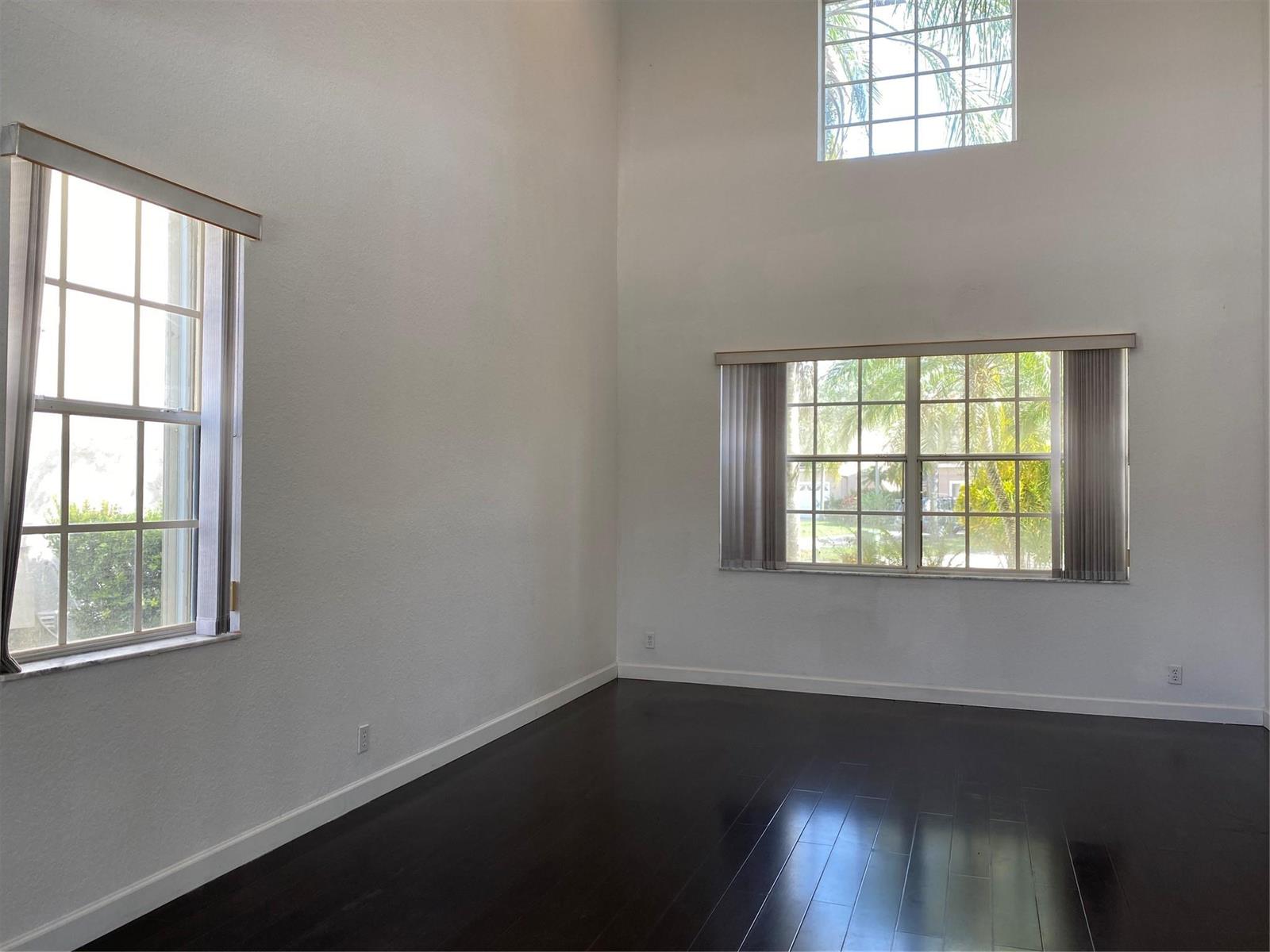 An empty room with dark wood floors, white walls, and multiple windows — 338 Cambridge Drive, Weston FL 33326, WESTON, FL